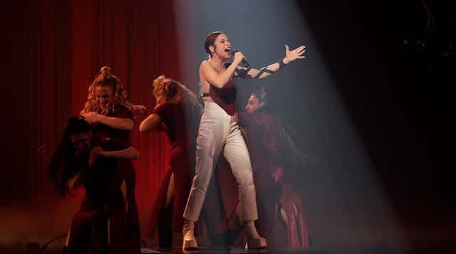 Una mujer canta en un escenario rodeada de mujeres que bailan flamenco.