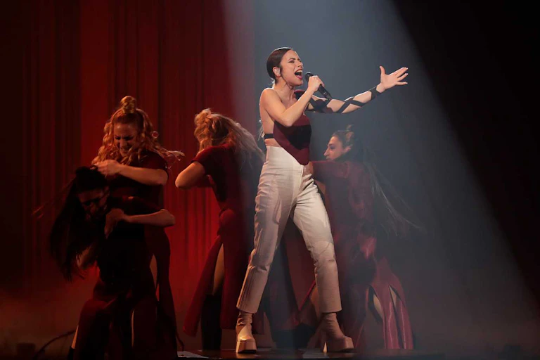 Una mujer canta en un escenario rodeada de mujeres que bailan flamenco.