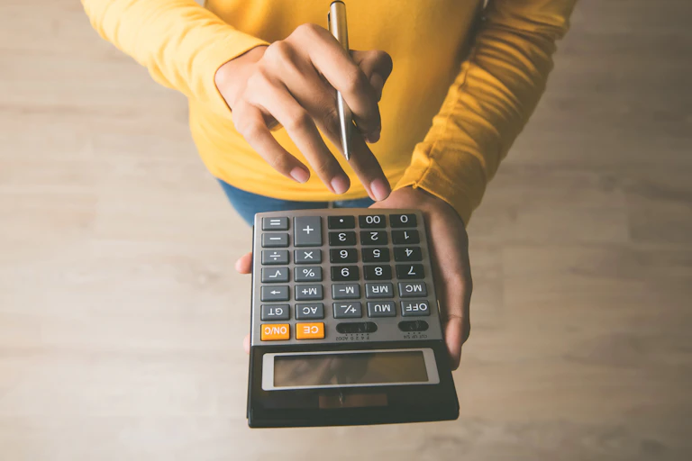 Woman using a calculator with a pen in her hand, calculating financial expense at home office