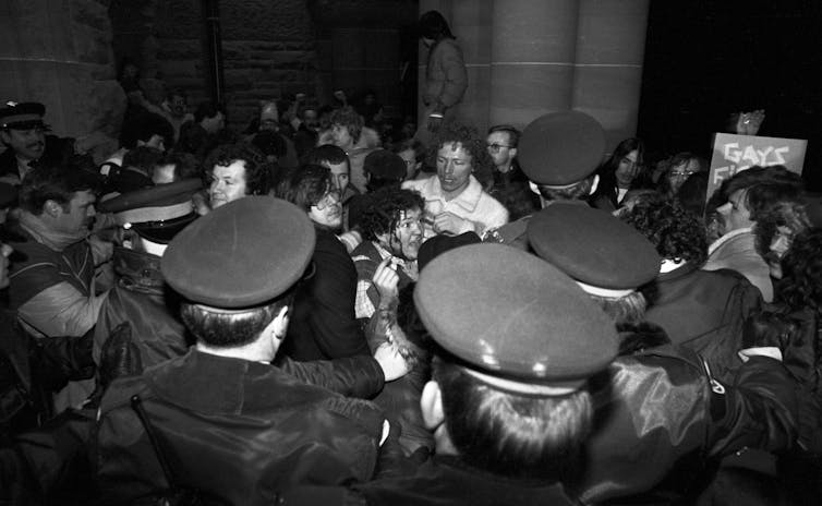 A black-and-white photo shows a man with blood on his face scuffling with a group of police officers.