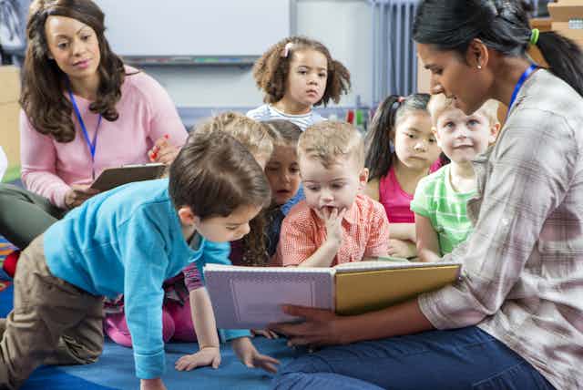 Children looking at book shown by teacher at nursery school