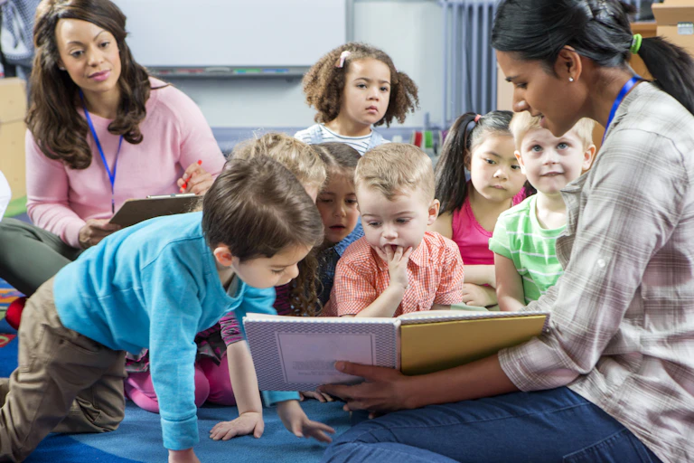 Children looking at book shown by teacher at nursery school