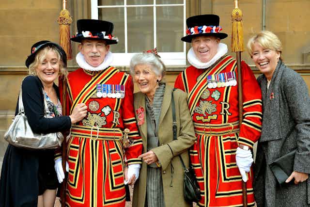 Actress Phyllida Law wears her OBE with actress daughters Sophie and Emma Thompson. They stand laughing with two men in Beefeater outfits. 