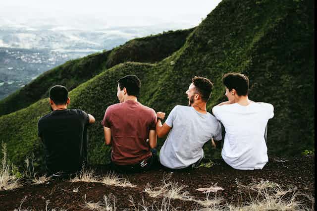 The back of four young men sitting on a hill.