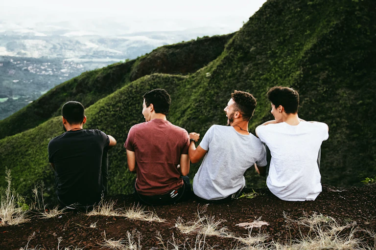 The back of four young men sitting on a hill.