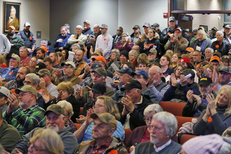 A lot of people applauding as they sit at a meeting.