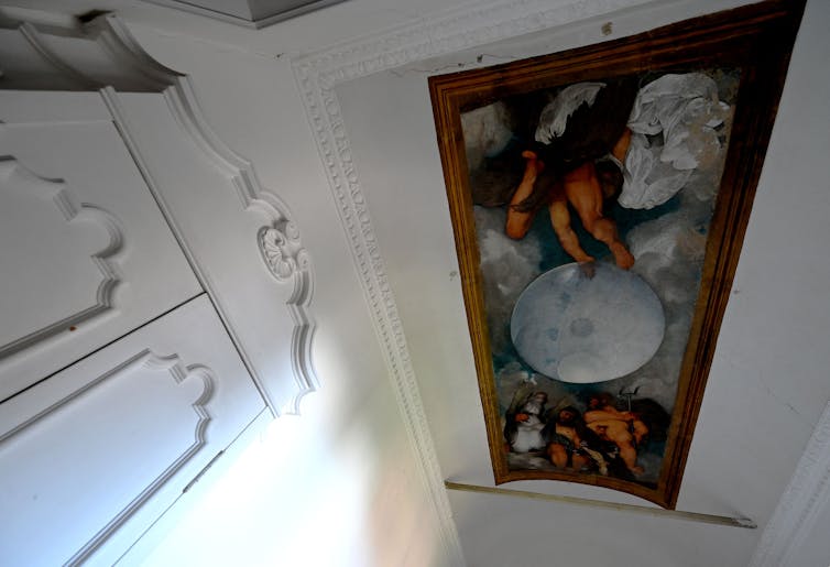 Ceiling painting of muscular men and mythological creatures surrounding an orb.
