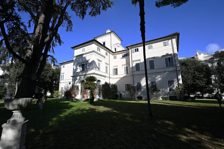 White mansion surrounded by lawn and trees.