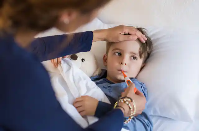 Sick boy in bed, mother with hand on forehead, inserting thermometer in his mouth