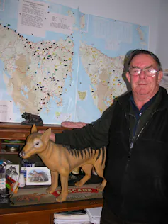 Man stands with his hand resting on a model of a thylacine