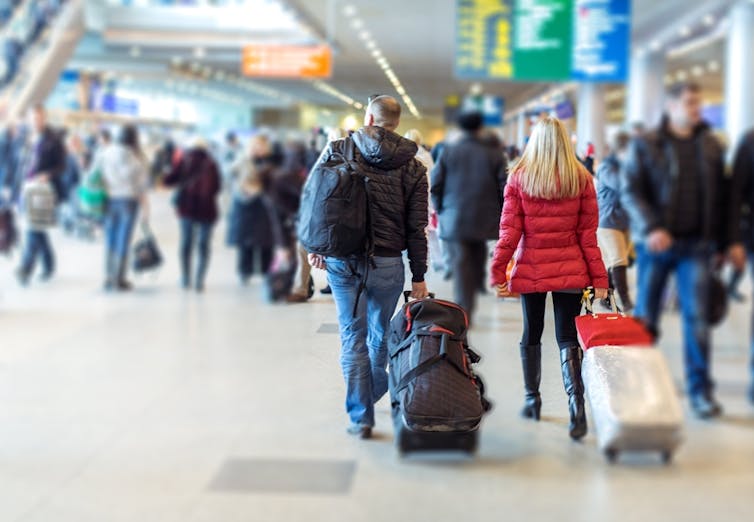 Travellers pulling roll-along luggage in busy airport