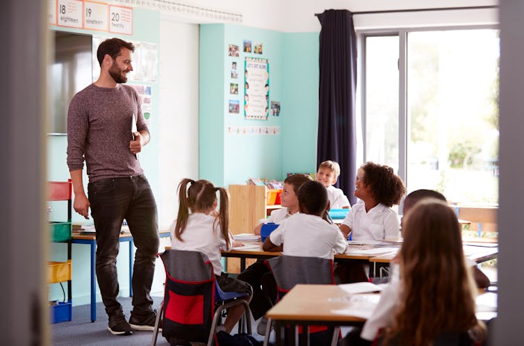 A teacher talks to young primary students in a classroom.