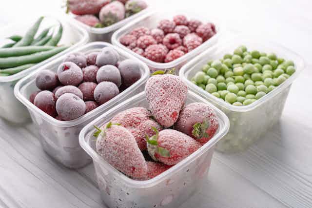 Six containers of frozen fruits and vegetables, including strawberries, peas, raspberries and green beans.