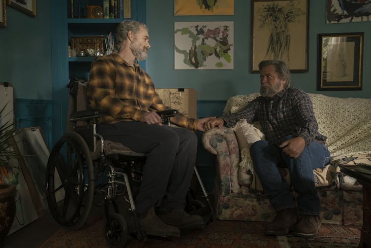 A man in wheelchair talks to a man on a sofa.