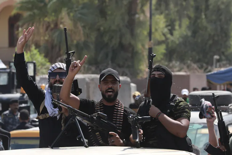 The armed men stand in a jeep wearing military uniforms.