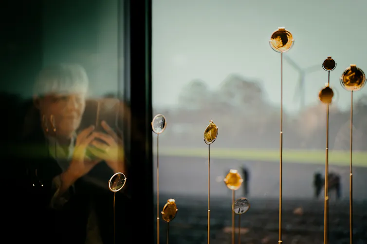 The gold pieces of The Vindelev hoard in a glass display cabinet. A woman takes a photograph from behind the glass.