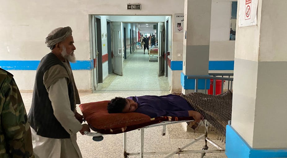 Man wheels another man lying on stretcher through a hospital