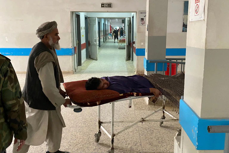Man wheels another man lying on stretcher through a hospital