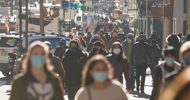A crowd of people walking a New York street wearing masks.