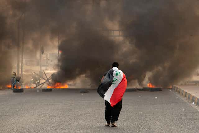 A man is seen walking with a black, red and white flag draped over his back as he walks toward a billow of smoke.