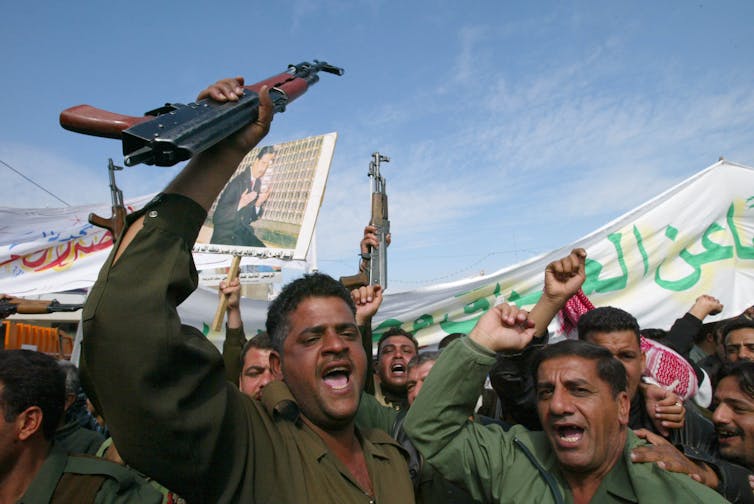 A group of men appear to be protesting in the street and raise Iraqi flags.