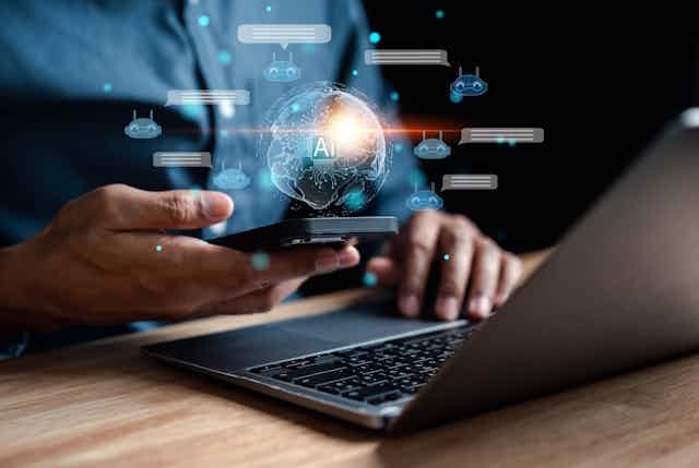 A person uses a cellphone while sitting in front of a laptop. A shining 3D image of the Earth hovers over the cellphone.