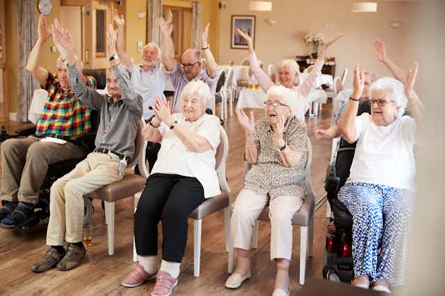 A group of elderly people seated with their hands raised high.