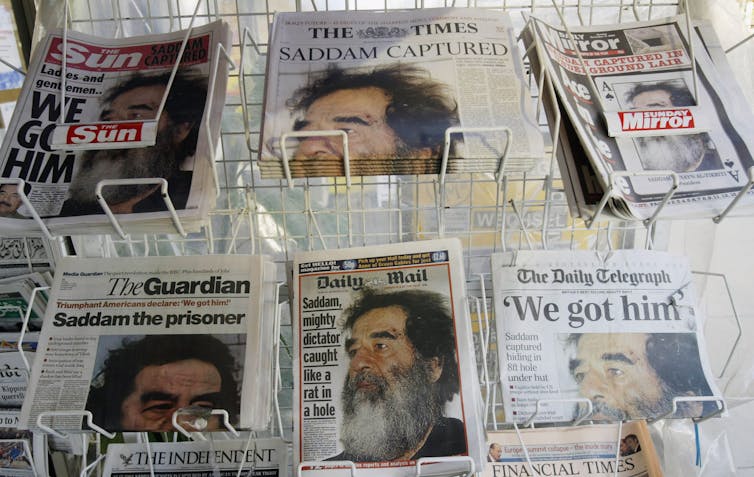 A row of newspapers show a bearded man with words like 'We got him' and 'Saddam captured.'