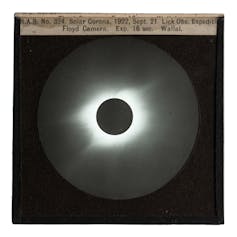 A photograph of the black totally eclipsed sun in the centre with a white haze of corona around it. The image was encapsulated in a glass plate slide to project for teaching at Sydney Observatory.