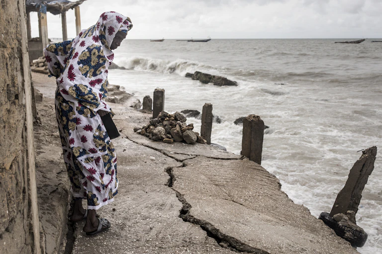 une femme regarde une fissure dans le sol à côté de la mer