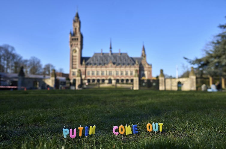 Candles that say 'Putin come out' on a large lawn in front of a stone courthouse.