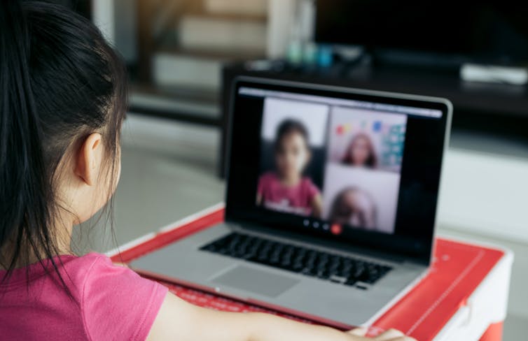 A young girl talks to other students on a laptop.