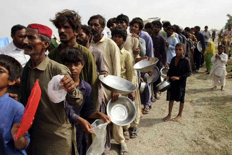 people hold bowls, queuing for food
