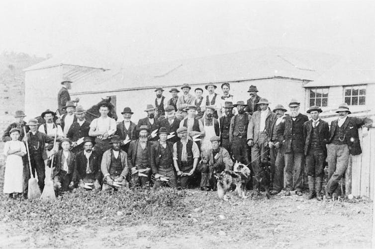 A photo of male farm workers gathered in front of a building.