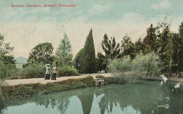 Two women in Victorian dress alongside a pond.