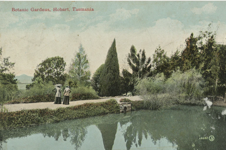 Two women in Victorian dress alongside a pond.