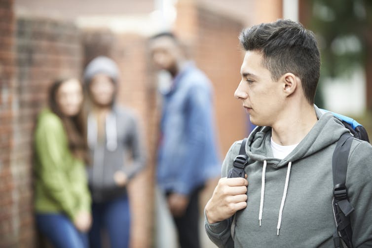 Young man looking anxious as he walks past group of young people