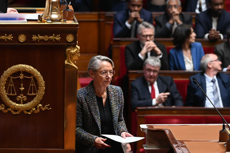 Des membres du Parlement de la coalition de gauche NUPES (Nouvelle Union Populaire Ecologique et Sociale) tiennent des pancartes alors que le Premier ministre français Elisabeth Borne (C) arrive pour confirmer l'adoption de la loi sur les retraites sans vote du Parlement lors d'une session sur la réforme des retraites du gouvernement à l'Assemblée nationale, à Paris, le 16 mars 2023.