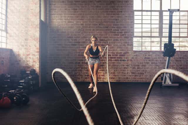 Mujer joven entrenando fuerza usando cuerdas pesadas en el gimnasio.