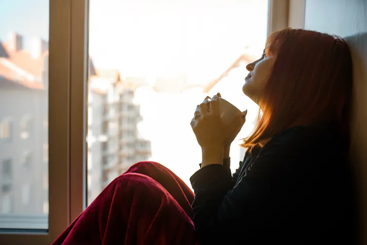Jeune femme assise devant une fenêtre et buvant un café avec un air triste