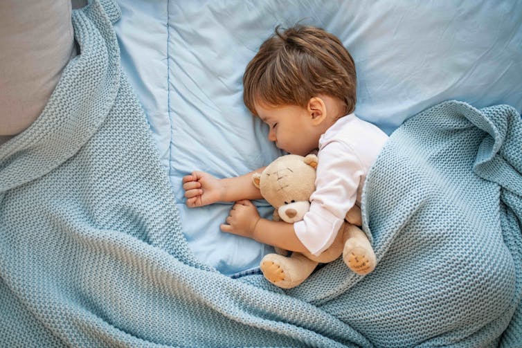 A little boy sleeps with a teddy bear.