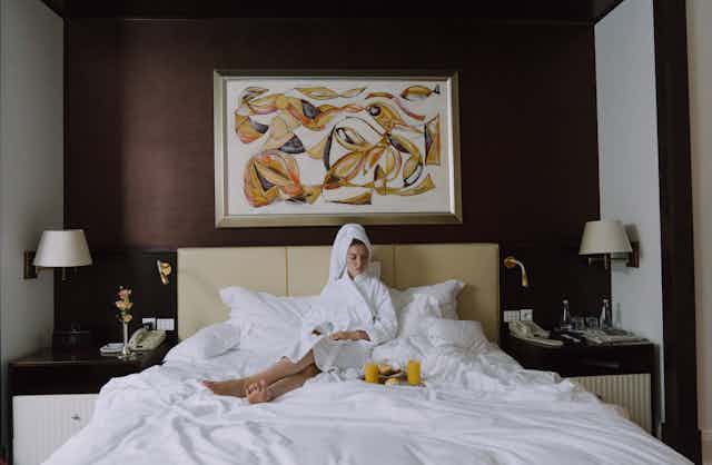 woman sitting on hotel bed in dressing gown.