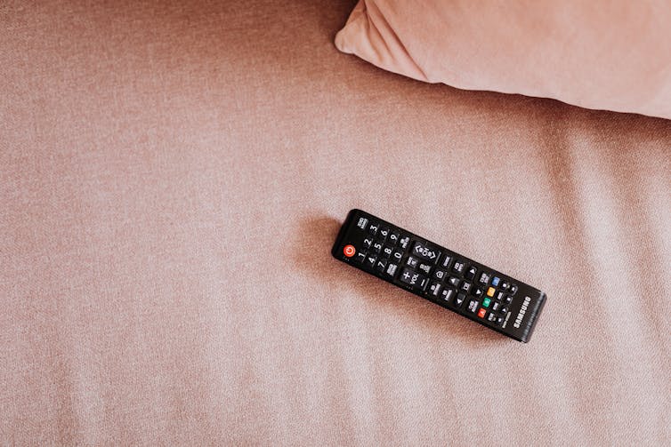 The TV remote is lying on the pink bed.