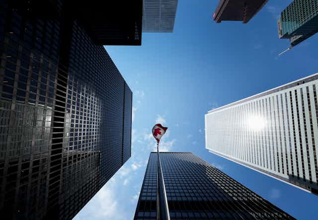 An upward shot of sky scrapers reaching toward the sky with a Canadian flag flying in the midst of them