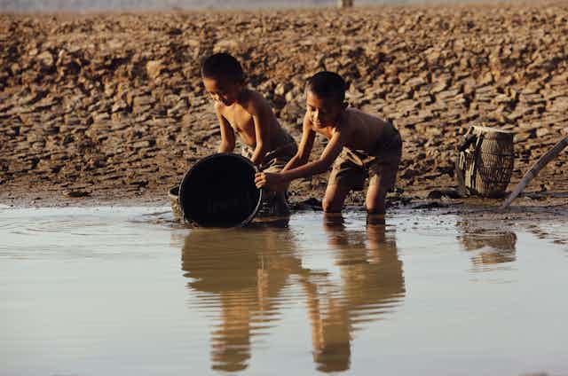 Dos niños asiáticos recogen agua en un río de agua turbia.