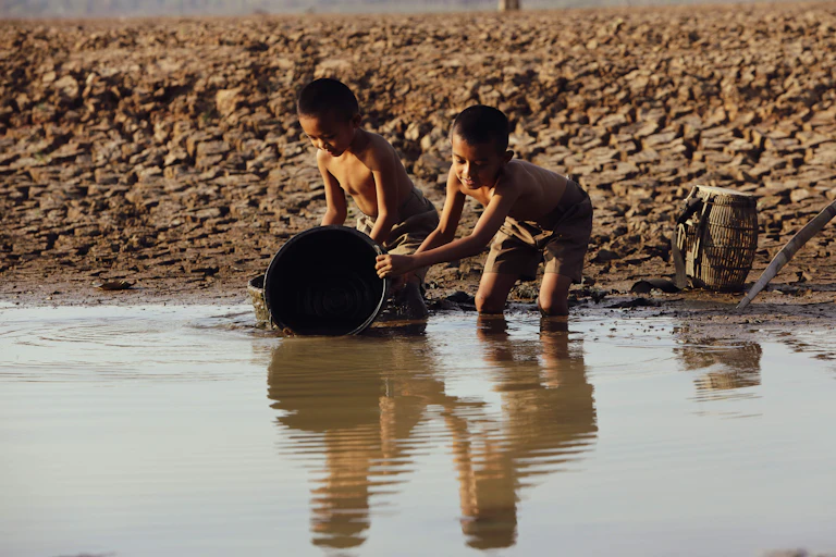 Dos niños asiáticos recogen agua en un río de agua turbia.