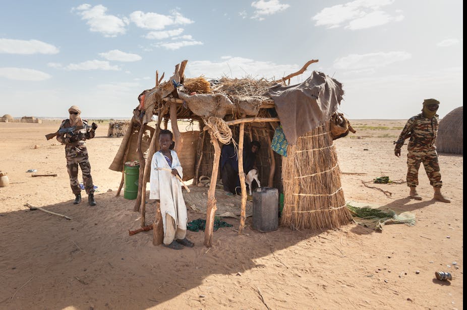 Des militaires patrouillent devant un abri pour bétail gardé par un enfant au Niger.