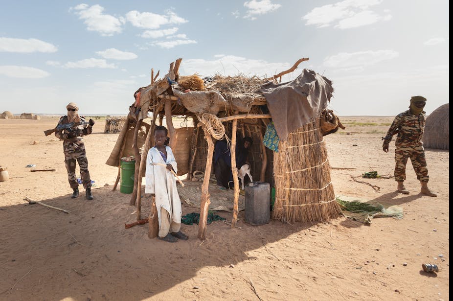 Des militaires patrouillent devant un abri pour bétail gardé par un enfant au Niger. 