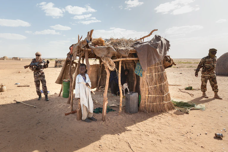 Des militaires patrouillent devant un abri pour bétail gardé par un enfant au Niger.