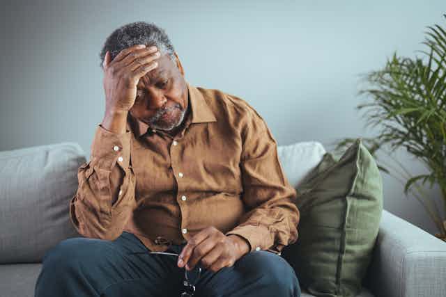 A middle-aged man sitting on a couch appears despondent.